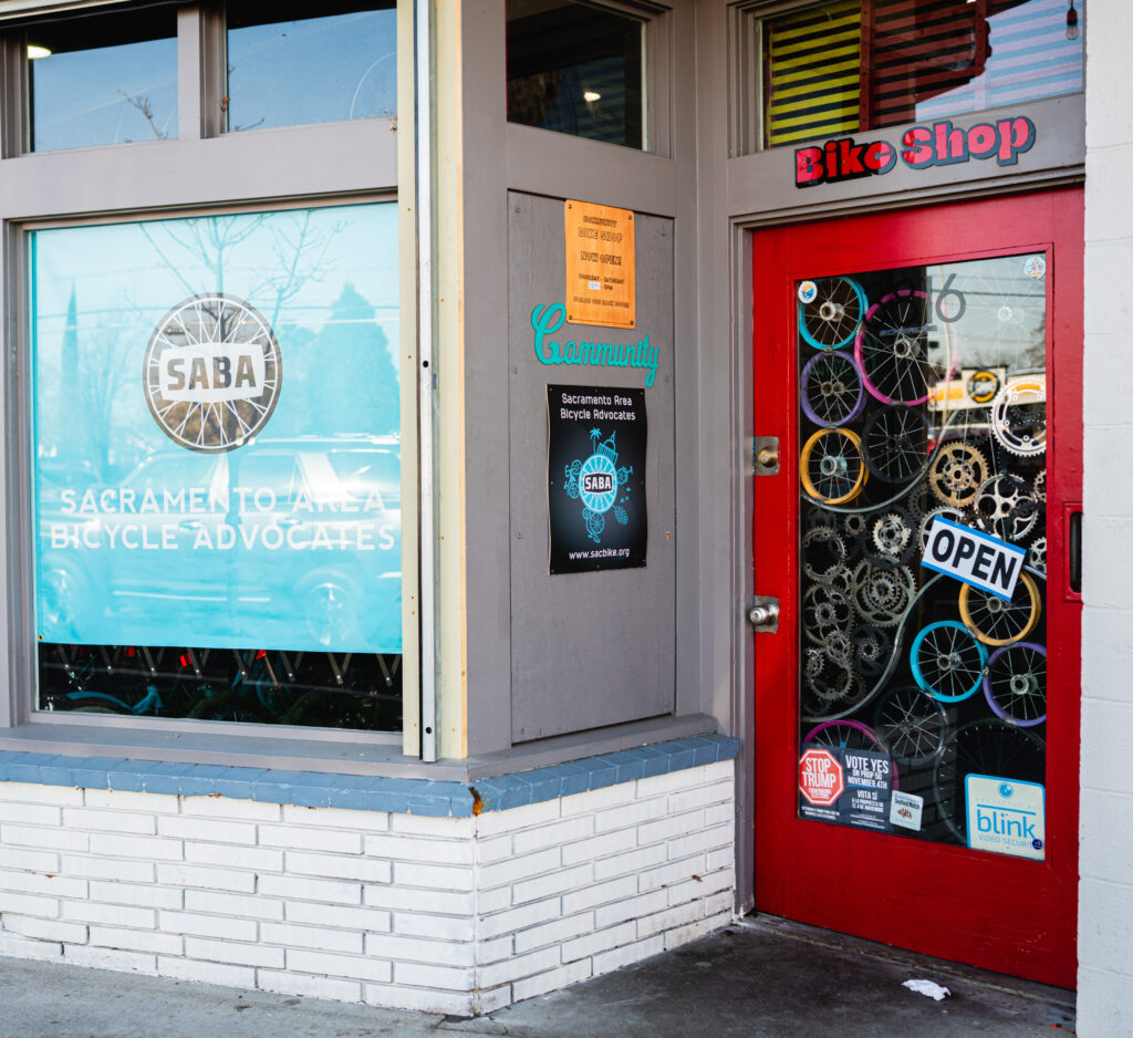 Community_Bike_Shop-9-crop Storefront with a SABA sign and a red trimmed glass door.