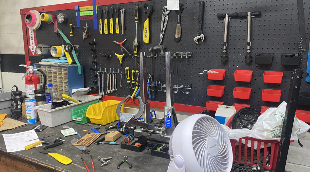 Various bike repair tools hang on a wall and are on a work bench.