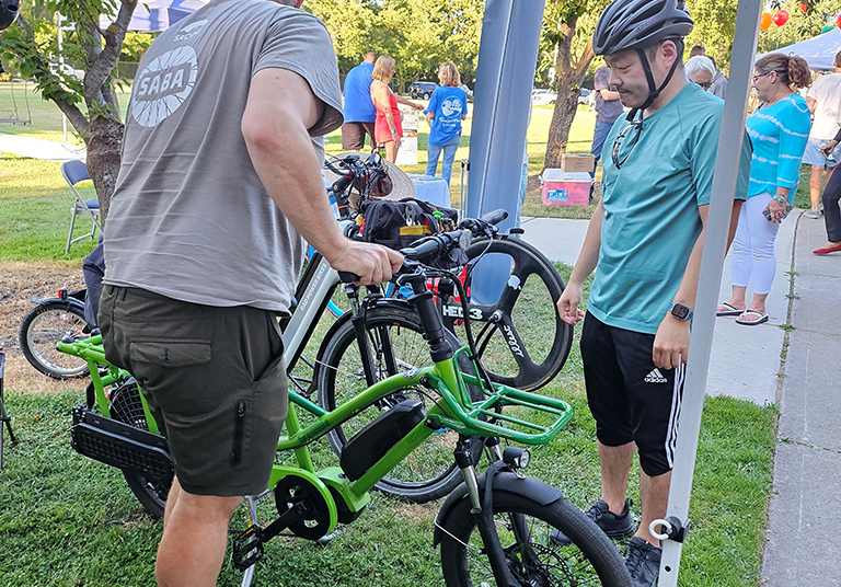 NNO e-bike 02-crop Two men look at an e-bike outside in a park.